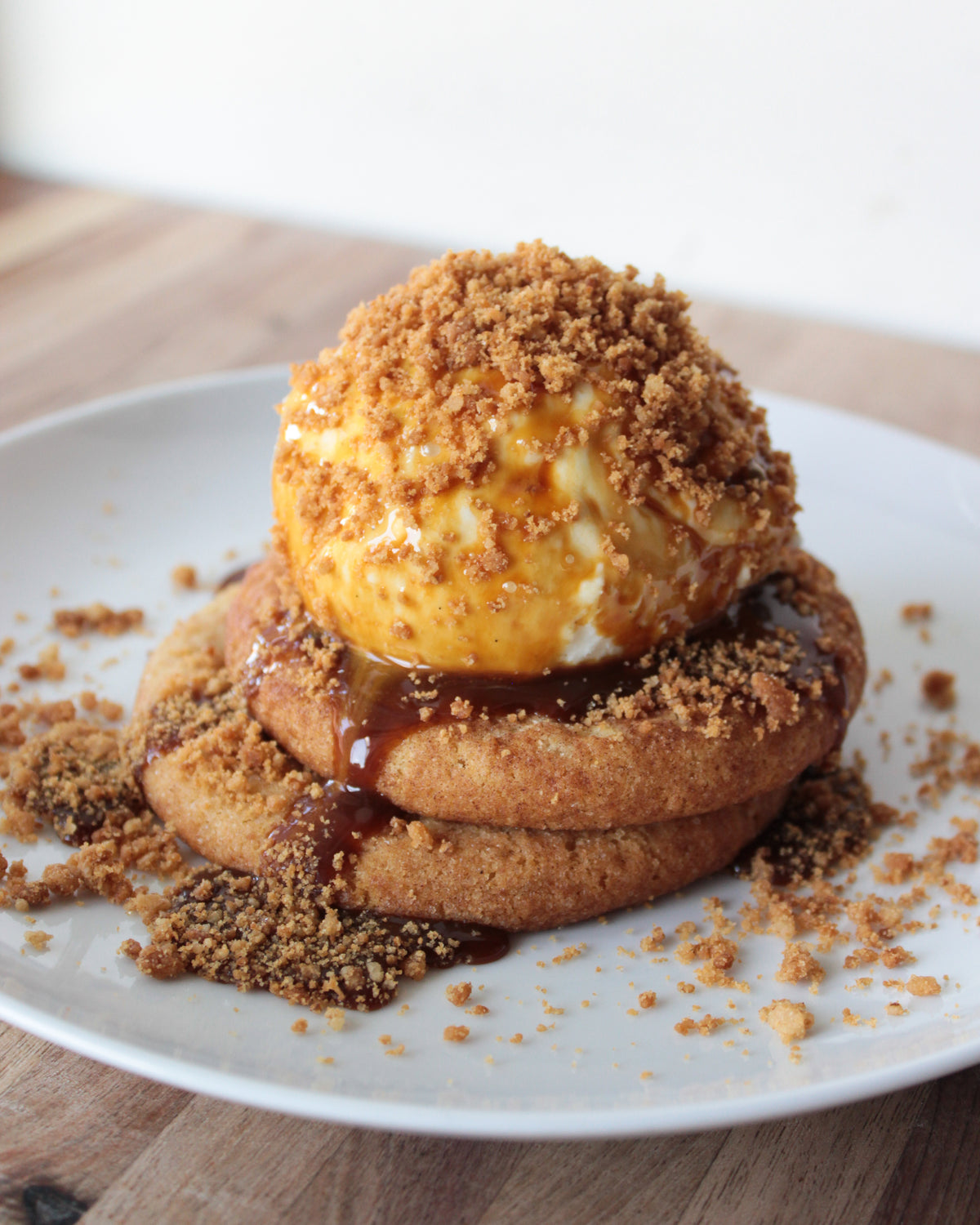 A dairy free dessert of two cookies & an ice cream scoop with a crumbly topping and vegan caramel sauce